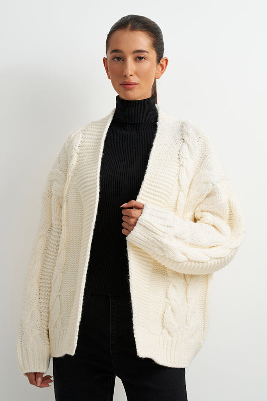 Woman wearing a cream cardigan over a black turtleneck on a white background