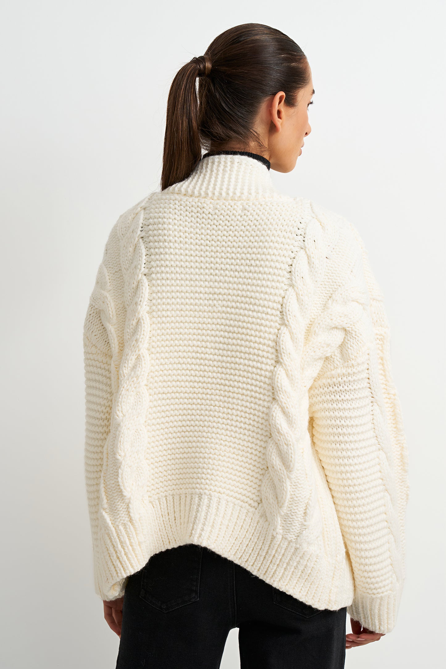 Person wearing a cream chunky knit sweater on a white background