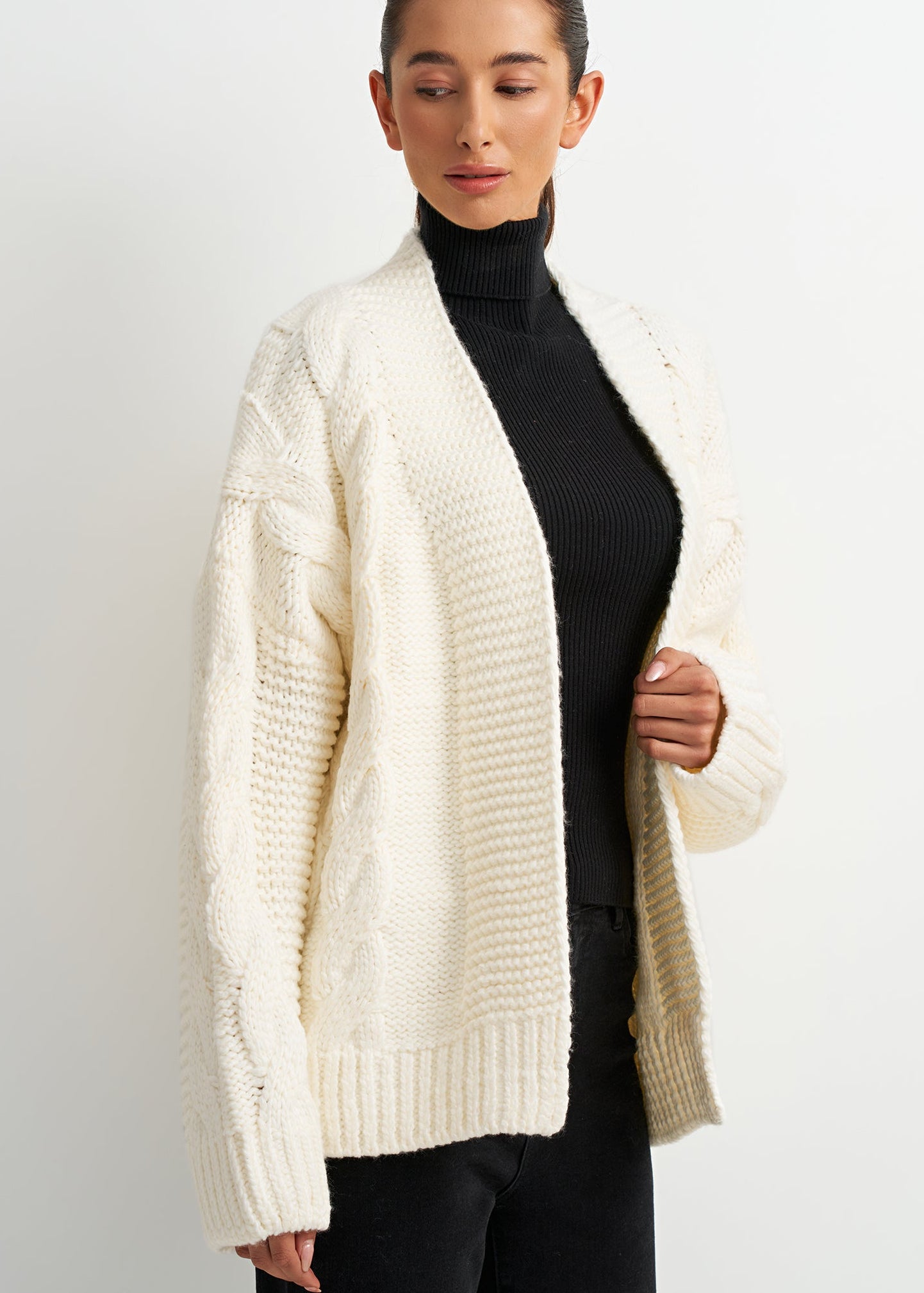 Woman wearing a cream cardigan over a black turtleneck on a white background