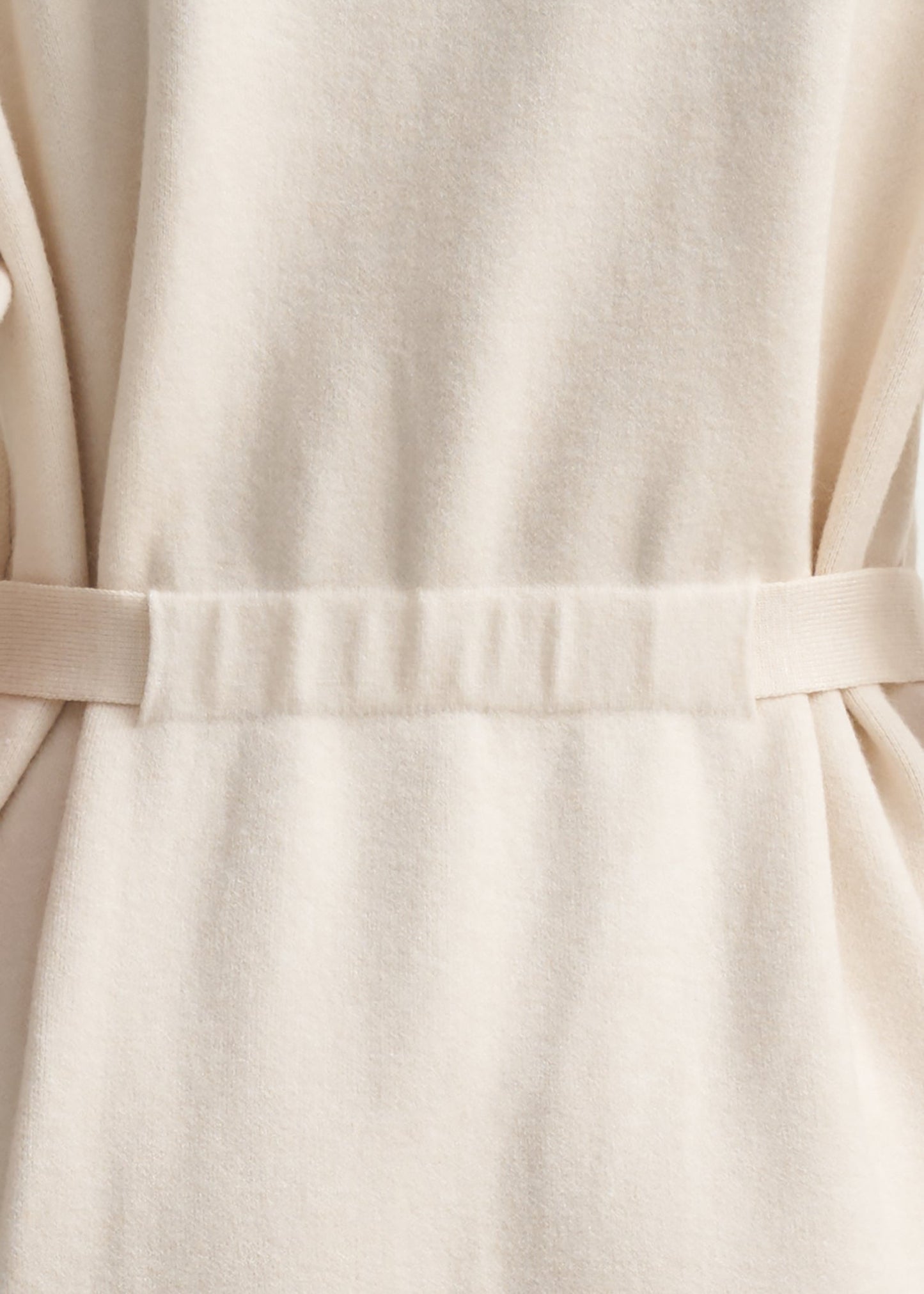 Close-up of a cream-colored fabric garment with a matching waist tie belt, showing the soft texture and folds of the material.