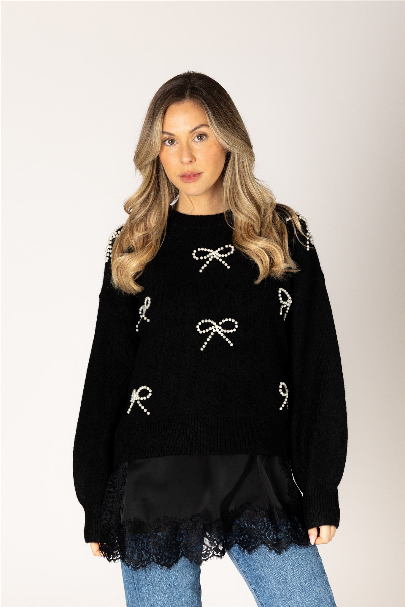 Woman wearing a black sweater with bow and letter designs on a plain background