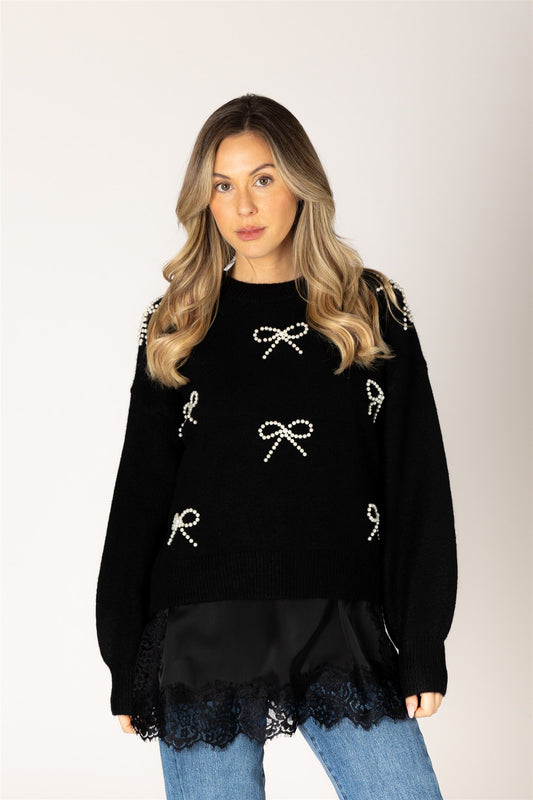 Woman wearing a black sweater with bow and letter designs on a plain background
