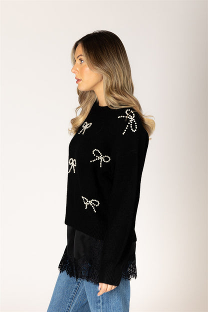 Woman wearing a black sweater with bow designs on a plain background