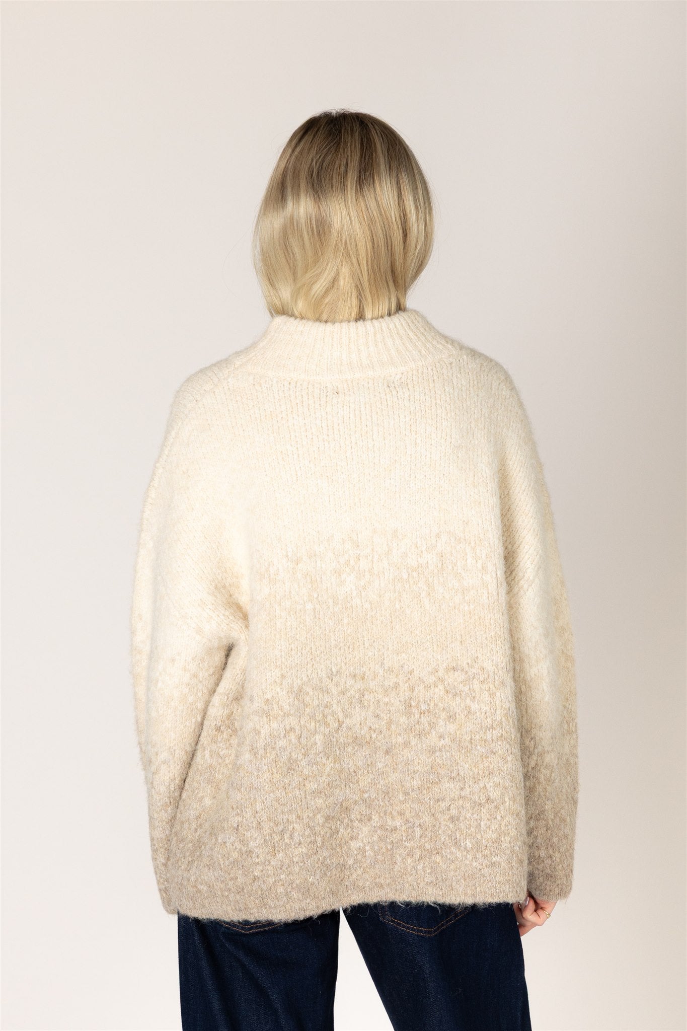 A person shown from the back wearing a fuzzy, textured cream-colored sweater and dark blue jeans against a plain light background.