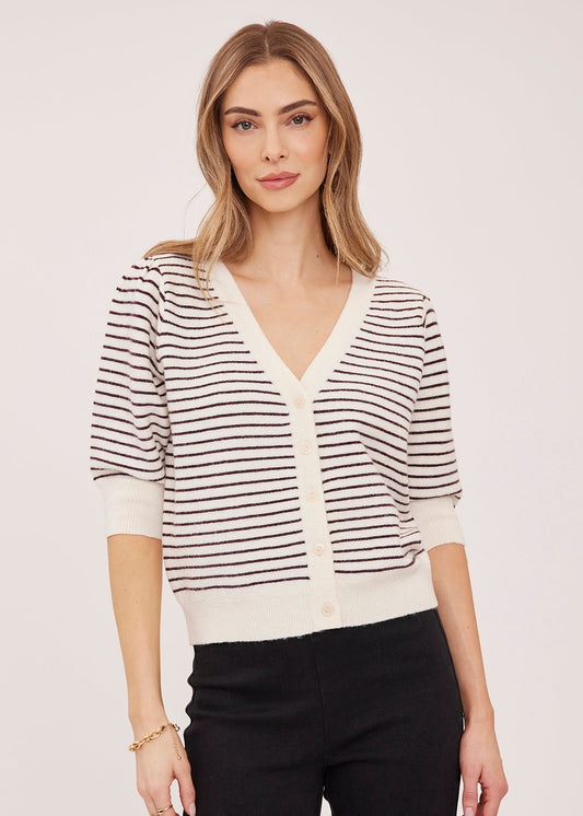 A woman modeling a short-sleeve knit cardigan with thin black horizontal stripes on an off-white base, paired with black pants, against a plain light gray studio background.