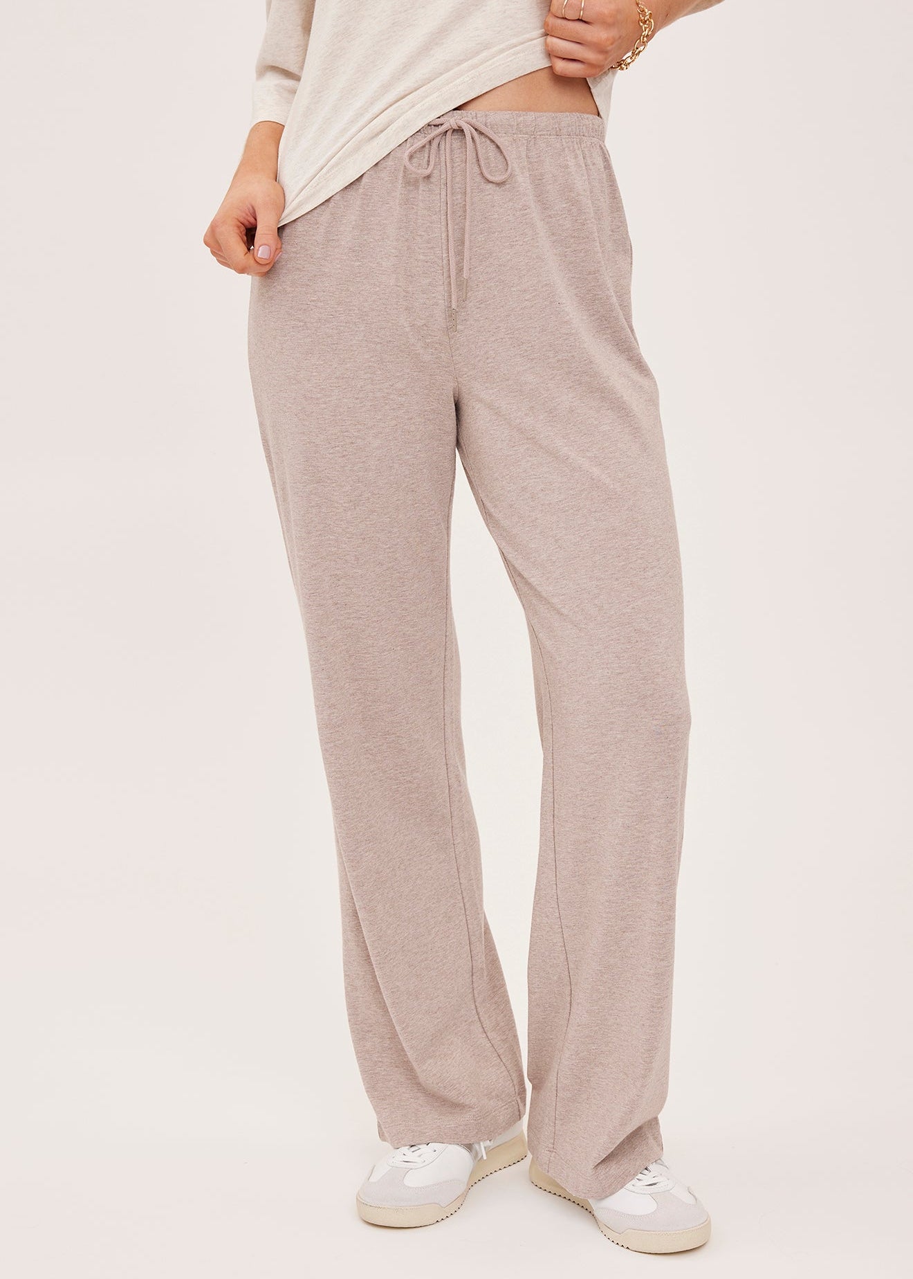 A person wearing light beige drawstring lounge pants with a cream long-sleeve top and white sneakers, shown from the chest down against a plain light background.