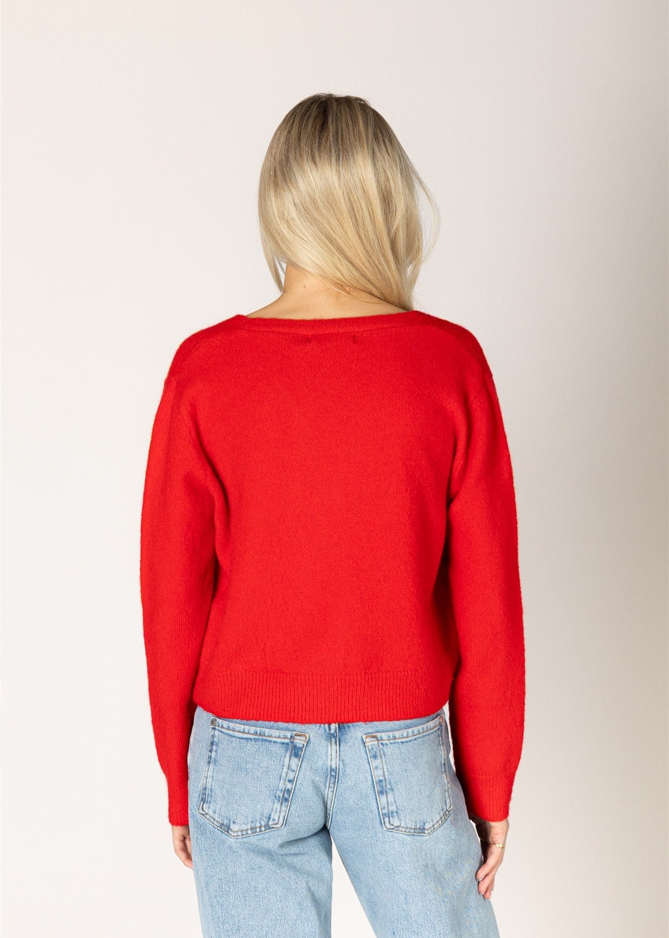 Person wearing a red sweater and light blue jeans on a plain background