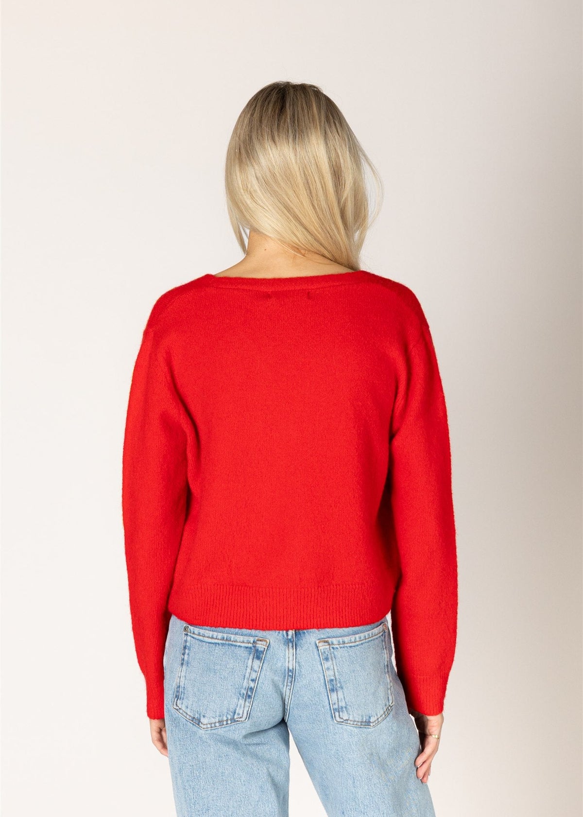 Person wearing a red sweater and light blue jeans on a plain background